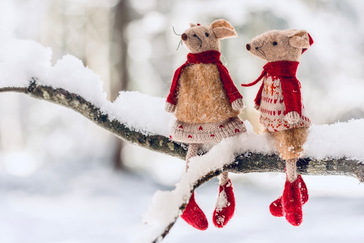 services-02 Charming mice dolls dressed in winter attire perched on a snow-covered branch outdoors.